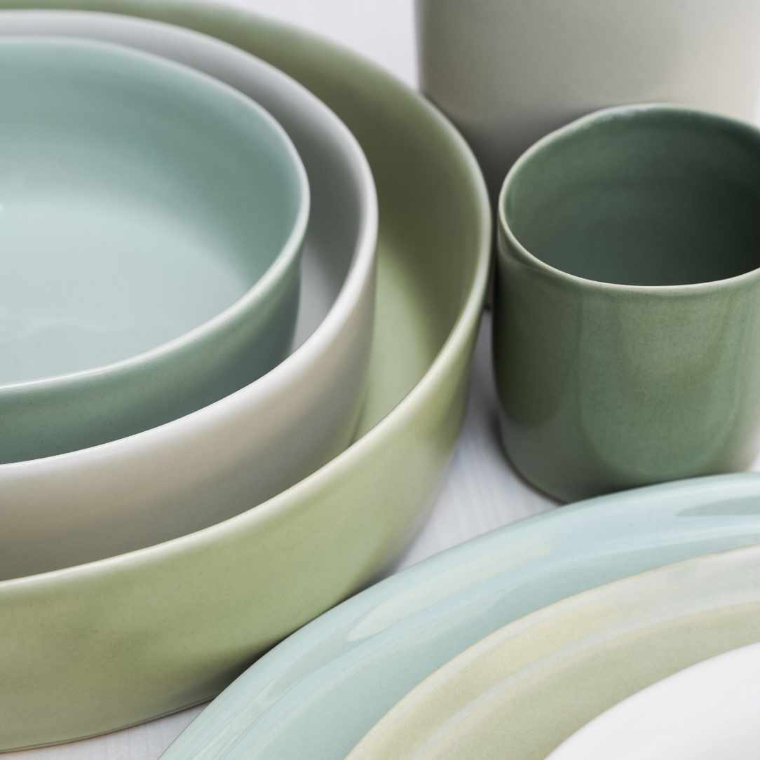 Grünes Keramik-Set aus Tellern, Schüsseln und einer Tasse in sanften Naturtönen auf hellem Hintergrund