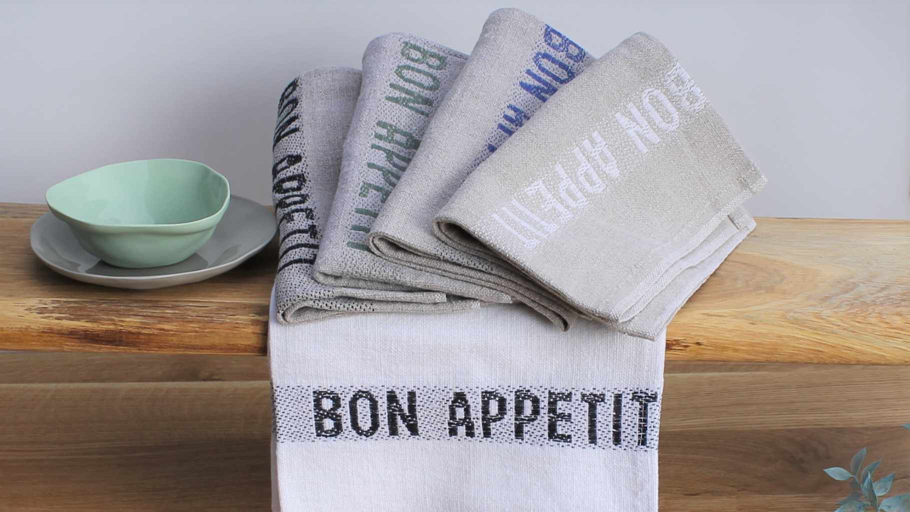 Leinenservietten in natur und weiß mit verschiedenfarbigen eingewebten Schriftzug "bon appetit".