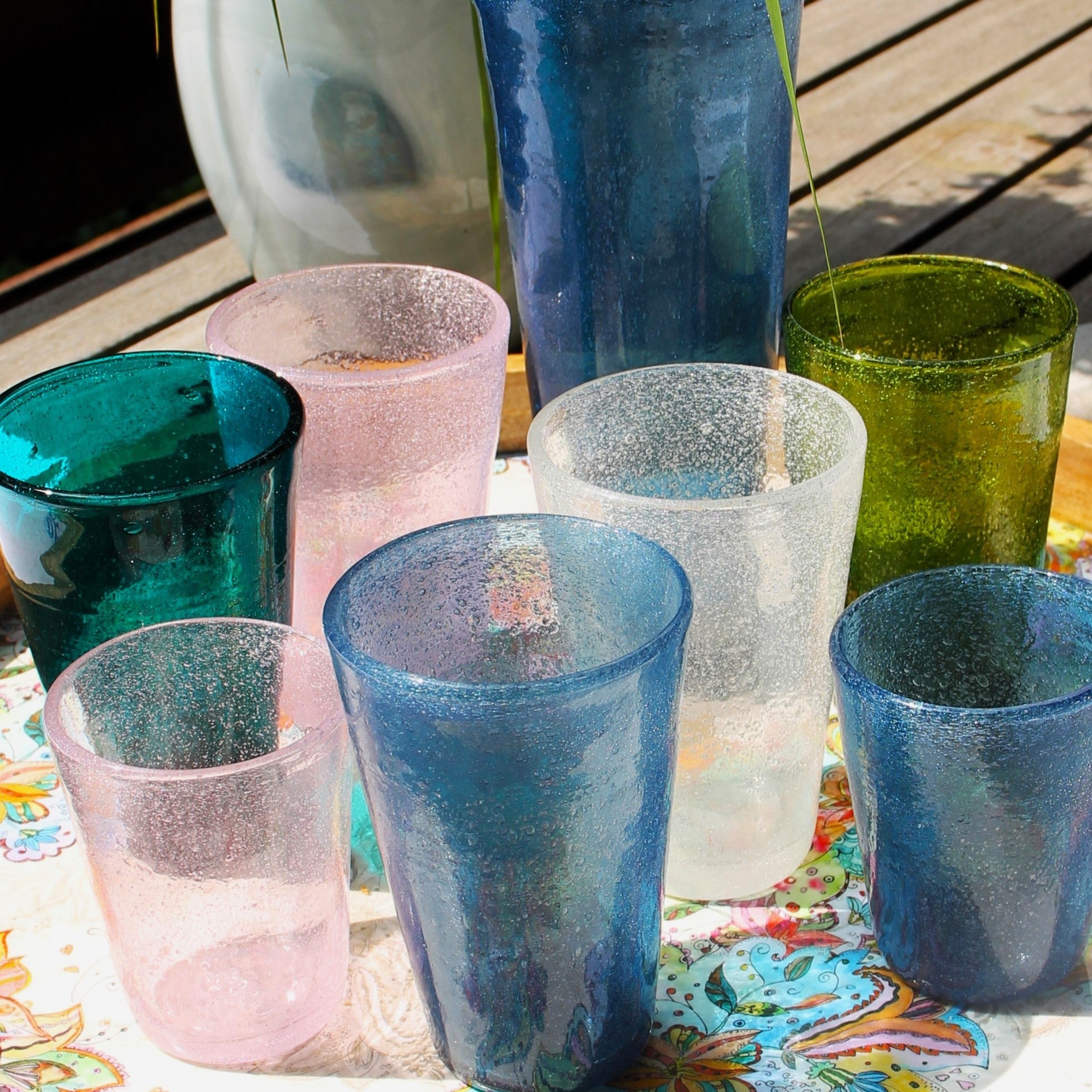 Große bunte mundgeblasene Gläser in verschiedenen Farben von Memento mit eingeschlossenen Luftbläschen. Darunter Blau, Grün, Rosa und weiß-transparent, auf einem dekorativen Tisch