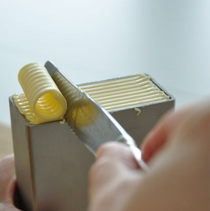 Butterdose aus Edelstahl, in der eine Person mit einem Messer eine Spirale Butter abschneidet