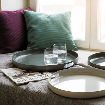 3 verschieden große  Emailletabletts in Gruentoenen auf Fensterbank vor Kissen.