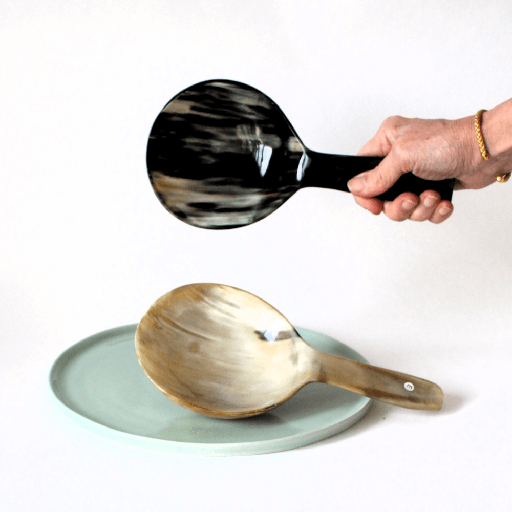 2  Schöpflöffel mit großer Laffe in unterschiedlichen Hornmaserungen . Einer in der Hand um die Abmessungen zu sehen, der andere auf einen mintfarbenen Teller liegend