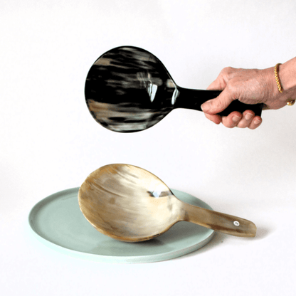 2  Schöpflöffel mit großer Laffe in unterschiedlichen Hornmaserungen . Einer in der Hand um die Abmessungen zu sehen, der andere auf einen mintfarbenen Teller liegend