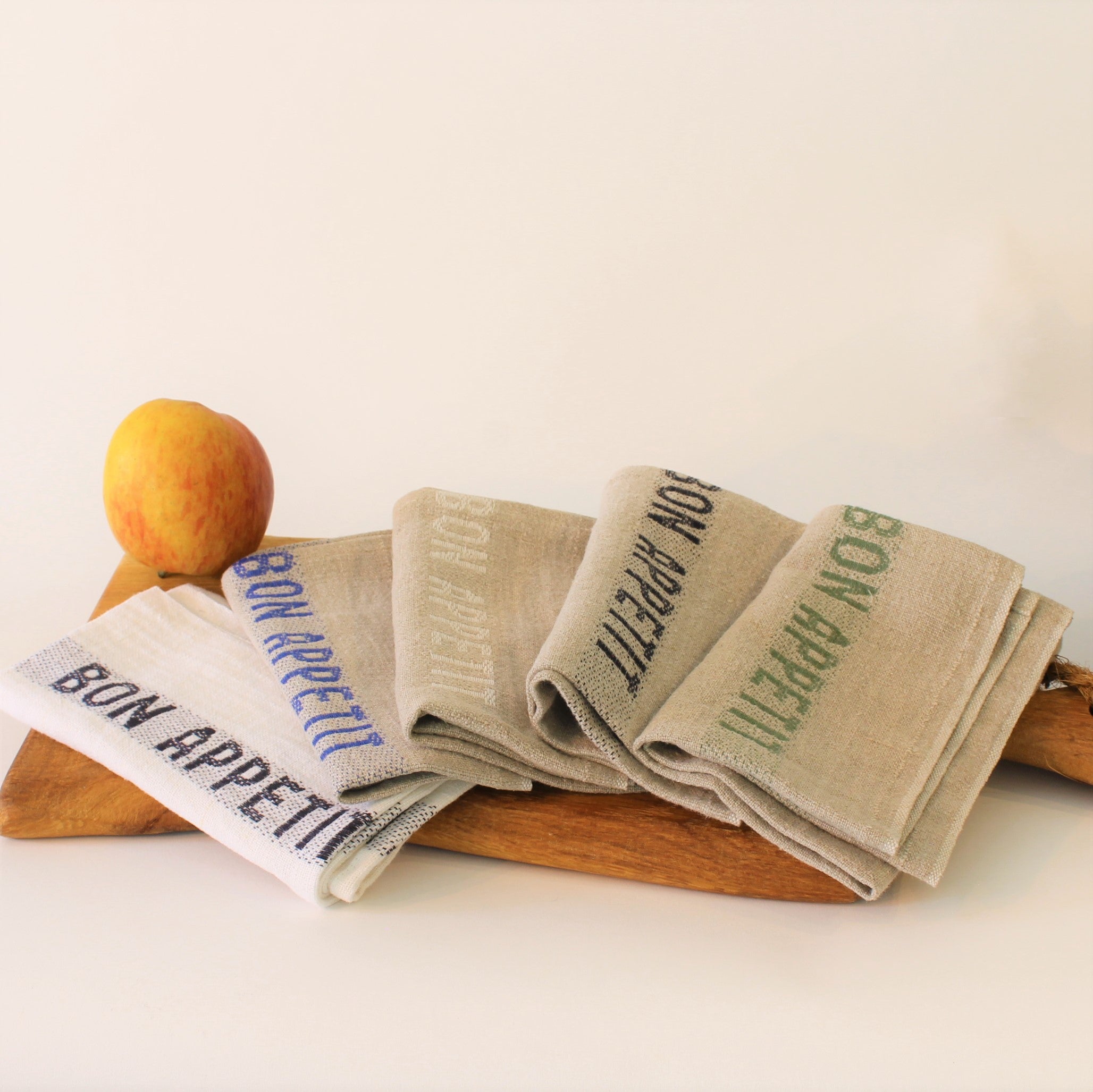 5 bunte Servietten Bon Appetit auf einem Eichenholzbrett dekoriert.  Leinen mit gewebten farbigen Schriftzug auf weiß- und naturfarbenen Grund  