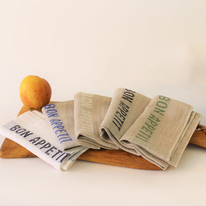 5 bunte Servietten Bon Appetit auf einem Eichenholzbrett dekoriert.  Leinen mit gewebten farbigen Schriftzug auf weiß- und naturfarbenen Grund  
